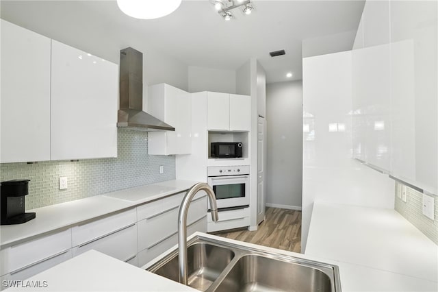 1000 L Ambiance Cir Unit 205, Naples, FL 34108 - kitchen featuring wall chimney range hood, black microwave, white oven, white cabinets, and tasteful backsplash