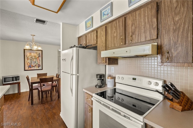 326 Canyon Dr N, Lehigh Acres, FL 33936 - kitchen with white appliances, under cabinet range hood, brown cabinetry, tasteful backsplash, and dark wood finished floors