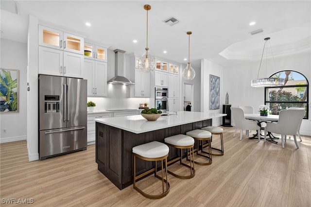 7637 Mulberry Ln, Naples, FL 34114 - kitchen featuring appliances with stainless steel finishes, wall chimney exhaust hood, light countertops, light wood-type flooring, and a kitchen island with sink