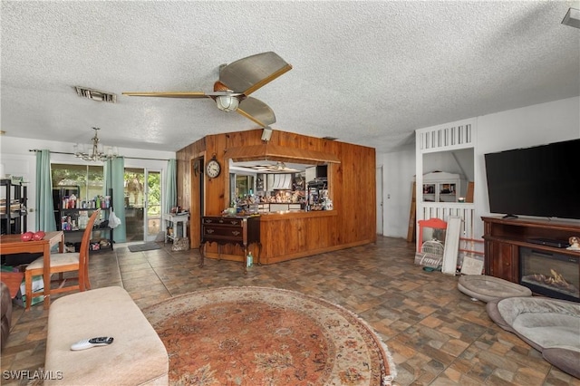 17041 Tarpon Way N, Fort Myers, FL 33917 - living area with a ceiling fan, a chandelier, a textured ceiling, wood walls, and a glass covered fireplace
