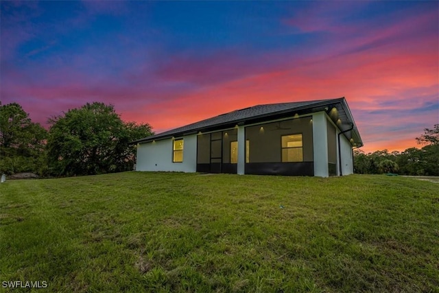1220 Edward Ave, Lehigh Acres, FL 33972 - back of property at dusk with stucco siding, a lawn, and a sunroom