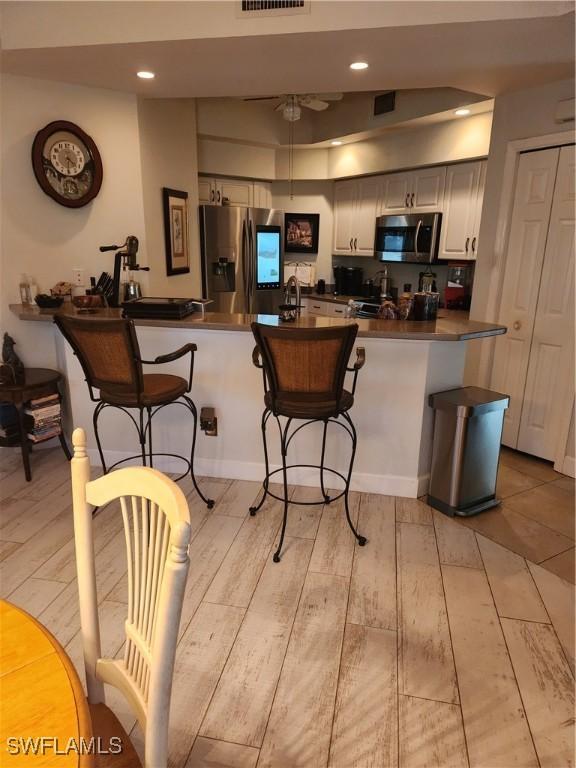 1240 Shady Rest Ln Unit 104, Naples, FL 34103 - kitchen with appliances with stainless steel finishes, dark countertops, a kitchen bar, light wood-type flooring, and a peninsula