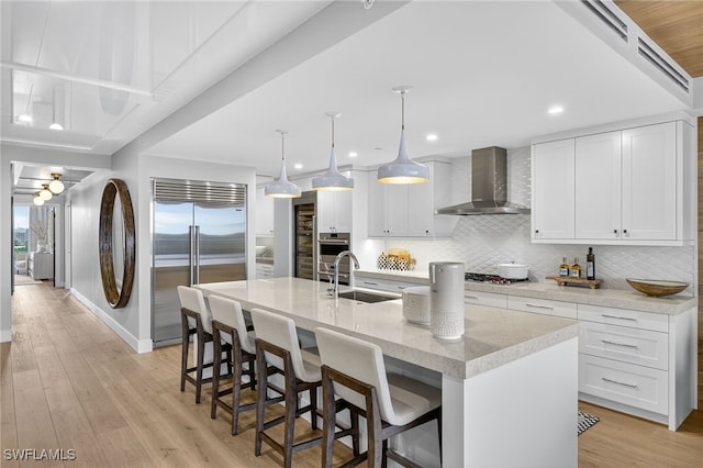 13925 Old Coast Rd Unit 403, Naples, FL 34110 - kitchen with built in fridge, wall chimney exhaust hood, backsplash, light wood-type flooring, and white cabinetry