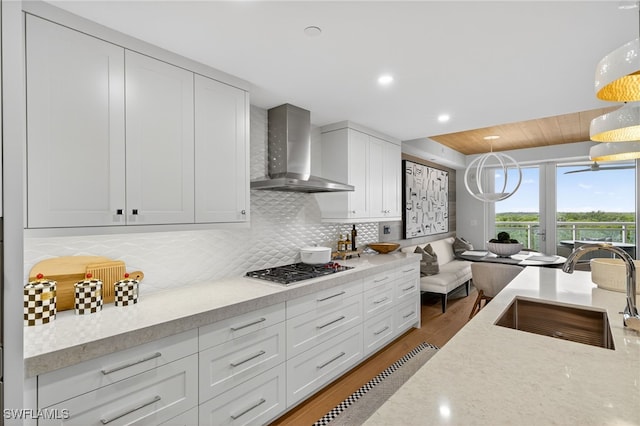 13925 Old Coast Rd Unit 403, Naples, FL 34110 - kitchen featuring wall chimney range hood, stainless steel gas cooktop, wood finished floors, white cabinetry, and backsplash