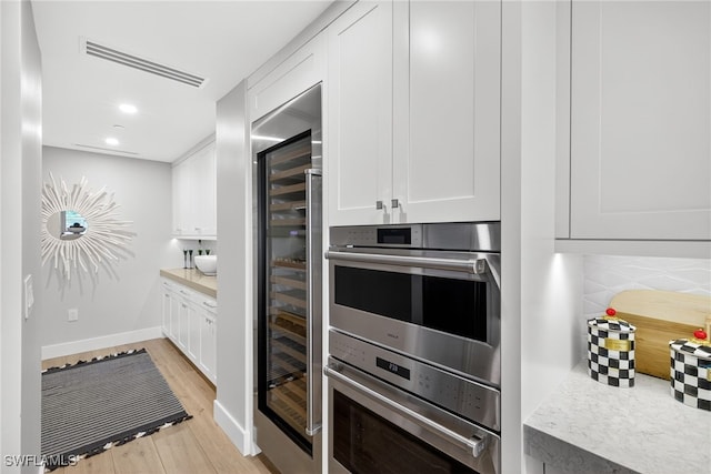 13925 Old Coast Rd Unit 403, Naples, FL 34110 - kitchen featuring light wood-style floors, beverage cooler, white cabinets, light countertops, and double oven