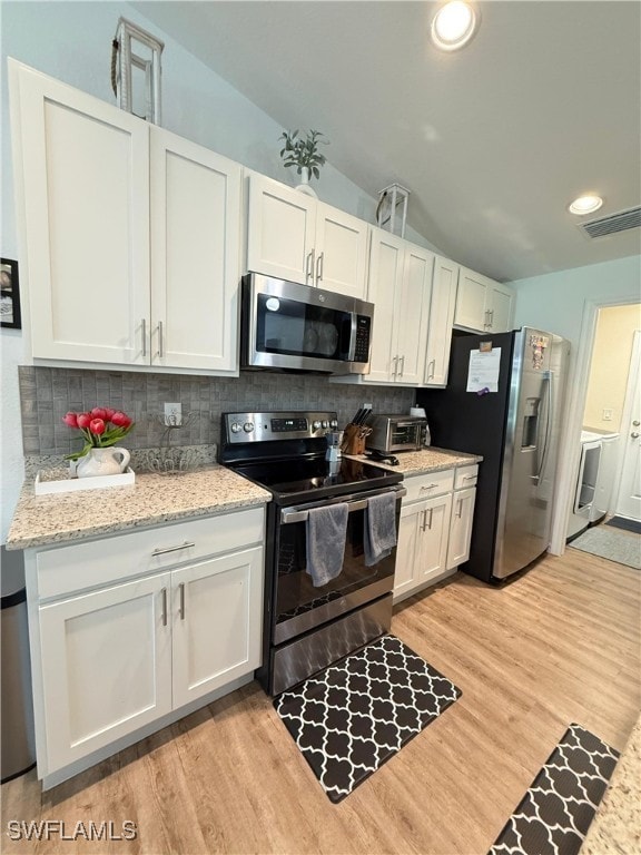 3006 Base Ct, Labelle, FL 33935 - kitchen with stainless steel appliances, vaulted ceiling, tasteful backsplash, light wood finished floors, and white cabinets