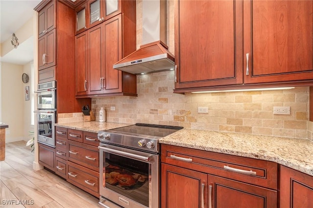 830 San Carlos Dr, Fort Myers Beach, FL 33931 - kitchen with appliances with stainless steel finishes, wall chimney range hood, light stone counters, brown cabinetry, and backsplash