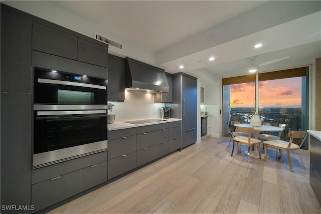 7515 Pelican Bay Blvd Unit 8A, Naples, FL 34108 - kitchen with wall chimney exhaust hood, stainless steel double oven, light wood-style floors, black electric cooktop, and light countertops