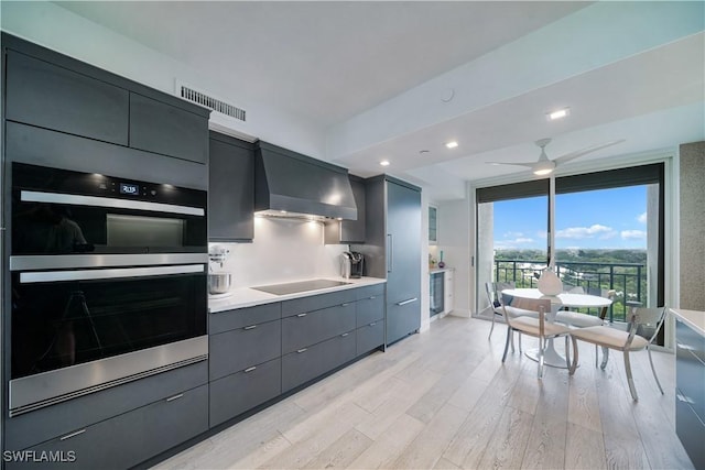 7515 Pelican Bay Blvd Unit 8A, Naples, FL 34108 - kitchen featuring wall chimney exhaust hood, double oven, black electric stovetop, light wood-style floors, and light countertops