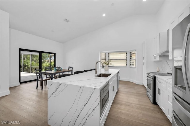 221 Saint James Way, Naples, FL 34104 - kitchen featuring appliances with stainless steel finishes, wall chimney range hood, vaulted ceiling, an island with sink, and white cabinets