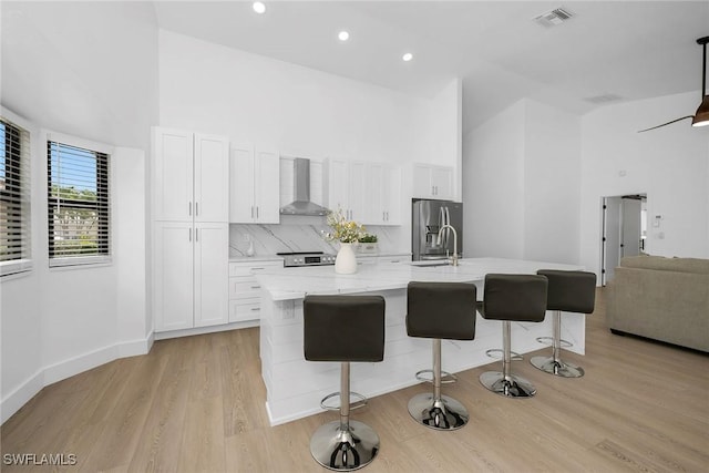 221 Saint James Way, Naples, FL 34104 - kitchen featuring wall chimney exhaust hood, stainless steel refrigerator with ice dispenser, white cabinetry, a kitchen island with sink, and high vaulted ceiling