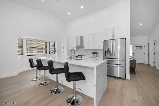 221 Saint James Way, Naples, FL 34104 - kitchen featuring stainless steel fridge with ice dispenser, high vaulted ceiling, wall chimney range hood, light wood-style flooring, and a kitchen island with sink