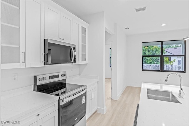 1061 Sunrise Blvd, Lehigh Acres, FL 33974 - kitchen with appliances with stainless steel finishes, light wood-style flooring, white cabinets, glass insert cabinets, and light stone counters
