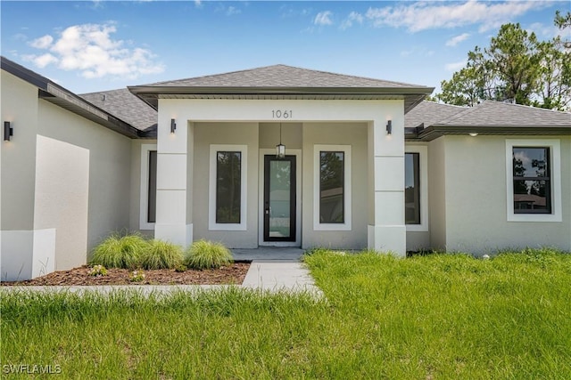 1061 Sunrise Blvd, Lehigh Acres, FL 33974 - entrance to property featuring a shingled roof, stucco siding, and a yard