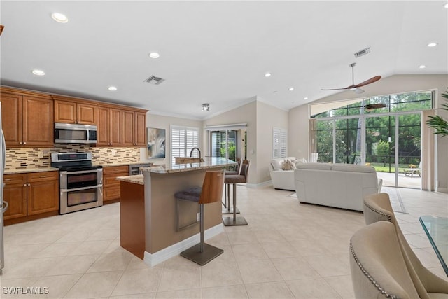 2434 Butterfly Palm Dr, Naples, FL 34119 - kitchen featuring stainless steel appliances, lofted ceiling, brown cabinetry, a kitchen breakfast bar, and decorative backsplash