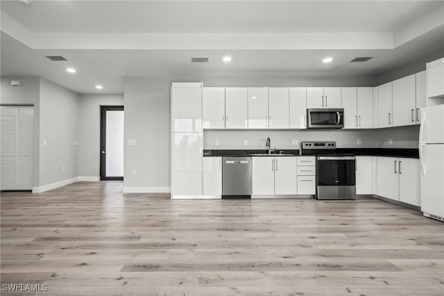 3006 72nd St W, Lehigh Acres, FL 33971 - kitchen with stainless steel appliances, recessed lighting, light wood-style flooring, dark countertops, and white cabinets