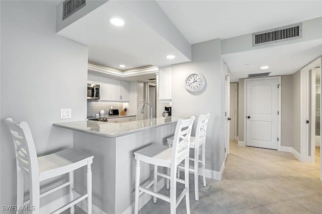 300 S Collier Blvd Unit 303, Marco Island, FL 34145 - kitchen featuring stainless steel microwave, recessed lighting, white cabinetry, a breakfast bar, and backsplash