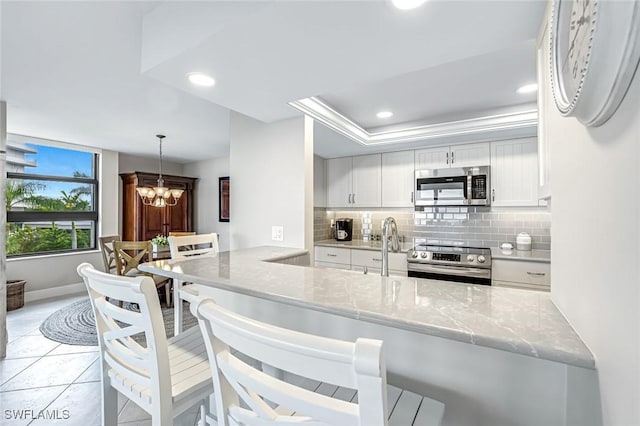 300 S Collier Blvd Unit 303, Marco Island, FL 34145 - kitchen featuring stainless steel appliances, backsplash, white cabinetry, a chandelier, and a peninsula