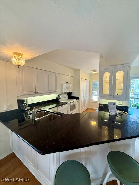 991 N Barfield Dr Unit 101, Marco Island, FL 34145 - kitchen with white appliances, a peninsula, a kitchen breakfast bar, dark wood finished floors, and dark countertops