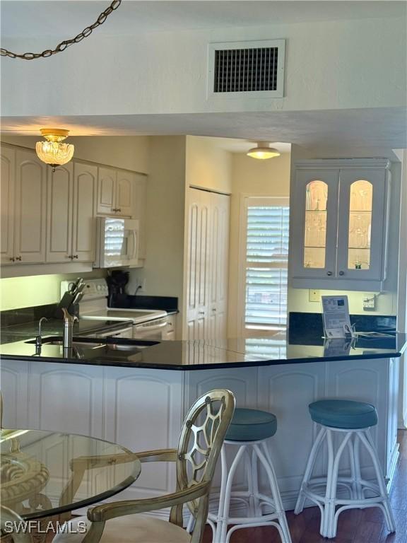991 N Barfield Dr Unit 101, Marco Island, FL 34145 - kitchen with white appliances, a peninsula, dark countertops, glass insert cabinets, and a kitchen breakfast bar