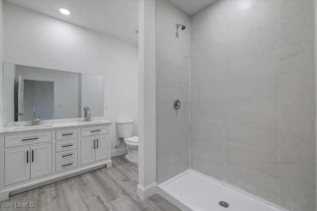 full bath featuring double vanity, wood finished floors, and tiled shower