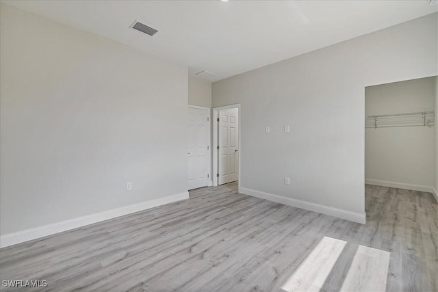 unfurnished bedroom featuring light wood-style floors, a walk in closet, and a closet