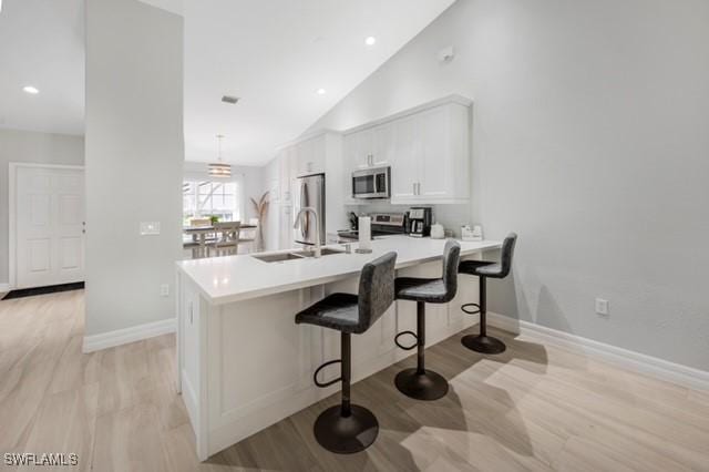3505 Avion Woods Ct Unit 902, Naples, FL 34104 - kitchen with appliances with stainless steel finishes, a kitchen breakfast bar, white cabinetry, light wood-type flooring, and high vaulted ceiling