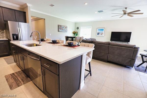 3393 Kacher Rd, North Port, FL 34288 - kitchen featuring stainless steel appliances, a kitchen bar, ornamental molding, dark brown cabinets, and light tile patterned floors