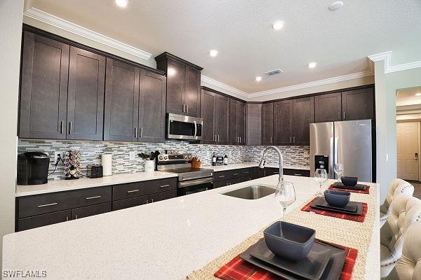 3393 Kacher Rd, North Port, FL 34288 - kitchen with appliances with stainless steel finishes, crown molding, decorative backsplash, dark brown cabinetry, and a breakfast bar
