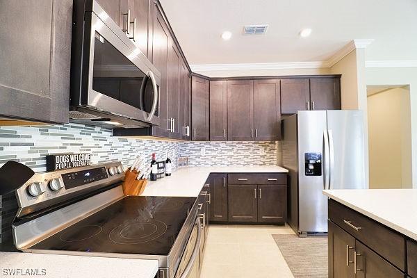 3393 Kacher Rd, North Port, FL 34288 - kitchen with stainless steel appliances, crown molding, dark brown cabinetry, decorative backsplash, and light countertops