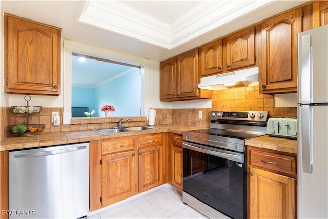 1014 Pine Isle Ln Unit 1014, Naples, FL 34112 - kitchen featuring stainless steel appliances, under cabinet range hood, ornamental molding, backsplash, and brown cabinets