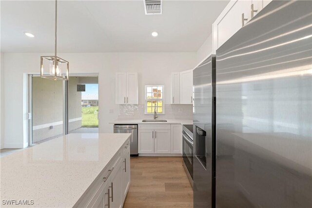 3111 11th St W, Lehigh Acres, FL 33971 - kitchen with appliances with stainless steel finishes, white cabinets, a chandelier, decorative backsplash, and light wood-style floors