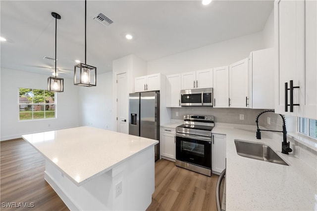 3109 11th St W, Lehigh Acres, FL 33971 - kitchen with stainless steel appliances, a kitchen island, light wood finished floors, decorative light fixtures, and decorative backsplash
