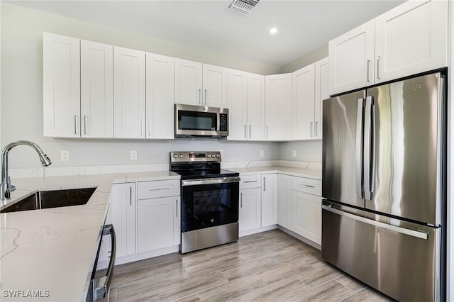 1909 Moore Ave, Lehigh Acres, FL 33972 - kitchen featuring stainless steel appliances, light stone countertops, white cabinetry, recessed lighting, and light wood-type flooring