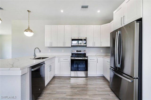 1909 Moore Ave, Lehigh Acres, FL 33972 - kitchen featuring stainless steel appliances, a peninsula, light stone counters, pendant lighting, and white cabinetry