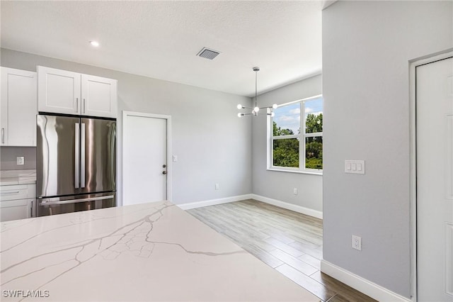 1909 Moore Ave, Lehigh Acres, FL 33972 - kitchen featuring freestanding refrigerator, wood finished floors, light stone countertops, a chandelier, and white cabinetry