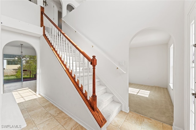 312 Lenz Ave S, Lehigh Acres, FL 33974 - stairs featuring arched walkways, a chandelier, tile patterned flooring, carpet floors, and a high ceiling