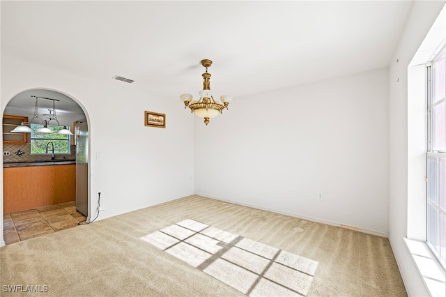 312 Lenz Ave S, Lehigh Acres, FL 33974 - spare room featuring light carpet, a chandelier, arched walkways, and plenty of natural light