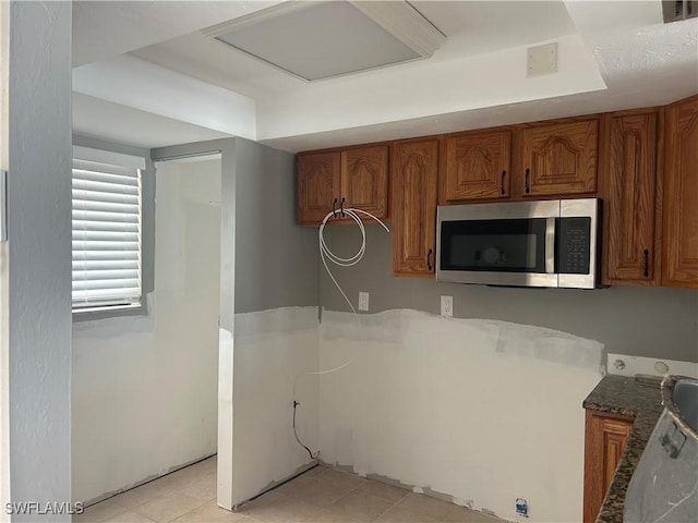 8350 Estero Blvd Unit 235, Fort Myers Beach, FL 33931 - kitchen featuring stainless steel microwave, brown cabinetry, dark stone countertops, and light tile patterned flooring