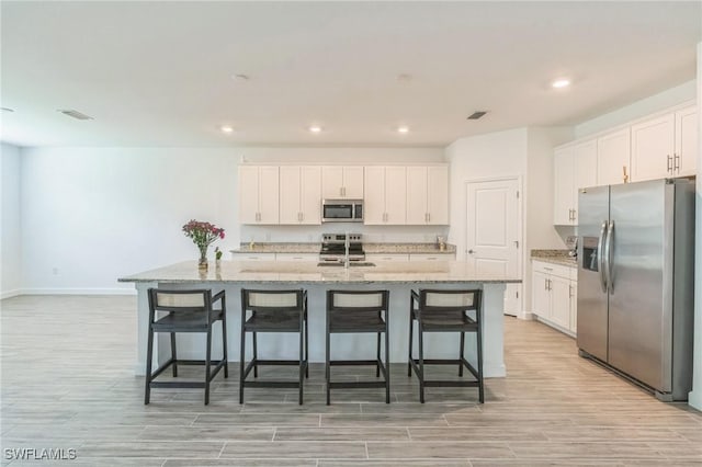 1801 Hagen Ct, Naples, FL 34120 - kitchen featuring appliances with stainless steel finishes, light wood finished floors, white cabinets, a kitchen breakfast bar, and recessed lighting