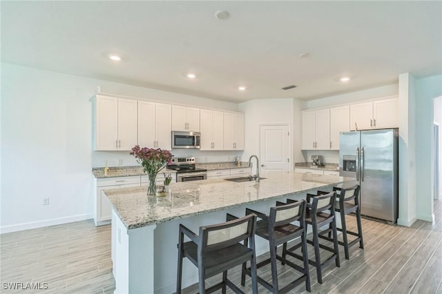 1801 Hagen Ct, Naples, FL 34120 - kitchen with stainless steel appliances, light wood-type flooring, white cabinetry, a kitchen bar, and recessed lighting