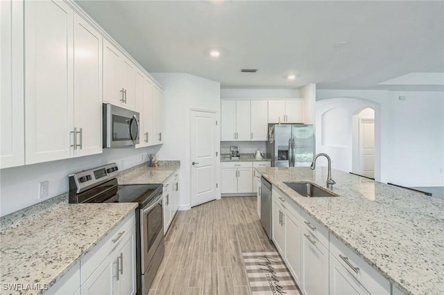 1801 Hagen Ct, Naples, FL 34120 - kitchen with stainless steel appliances, arched walkways, white cabinets, light stone countertops, and recessed lighting