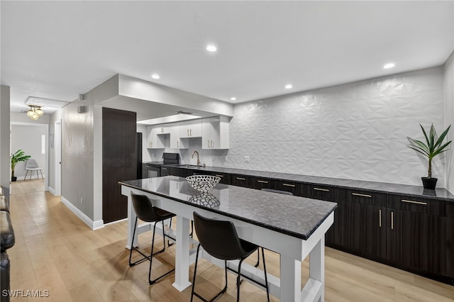 610 SW 47th Ter Unit 2, Cape Coral, FL 33914 - kitchen featuring a breakfast bar area, dark cabinets, tasteful backsplash, light wood finished floors, and dark stone counters