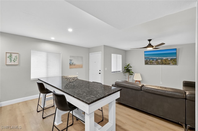 610 SW 47th Ter Unit 2, Cape Coral, FL 33914 - kitchen featuring light wood-style flooring, a breakfast bar, a kitchen island, a ceiling fan, and dark stone counters