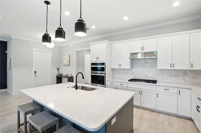 8951 Saint Lucia Dr, Naples, FL 34114 - kitchen with stainless steel double oven, gas stovetop, under cabinet range hood, a breakfast bar area, and white cabinets