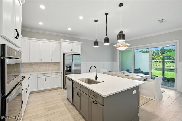 8951 Saint Lucia Dr, Naples, FL 34114 - kitchen featuring appliances with stainless steel finishes, ornamental molding, white cabinets, an island with sink, and decorative light fixtures