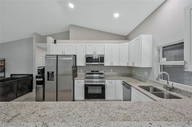 1417 Acacia Ave, Lehigh Acres, FL 33972 - kitchen featuring stainless steel appliances, vaulted ceiling, light stone counters, white cabinets, and wood finished floors