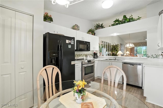 800 New Waterford Dr Unit A202, Naples, FL 34104 - kitchen with black appliances, light countertops, white cabinetry, light wood-type flooring, and hanging light fixtures