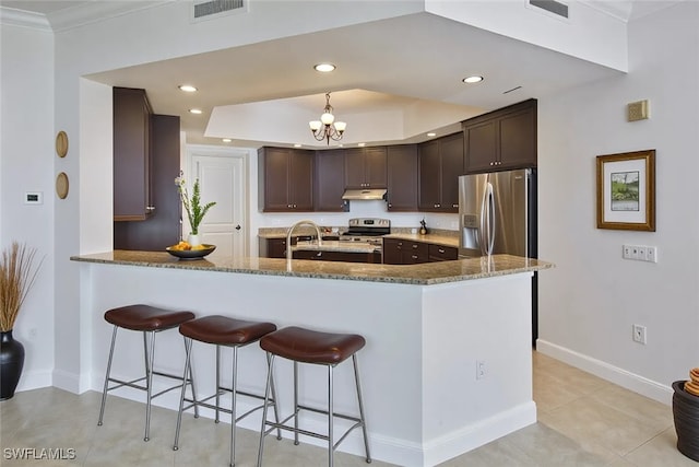 24011 Via Castella Dr Unit 2402, Bonita Springs, FL 34134 - kitchen with stainless steel appliances, under cabinet range hood, dark brown cabinets, a peninsula, and light stone counters
