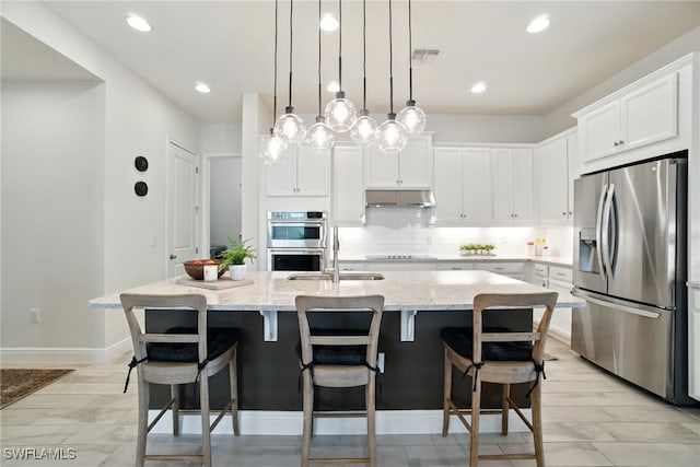 3387 Pilot Cir, Naples, FL 34120 - kitchen featuring appliances with stainless steel finishes, under cabinet range hood, light stone countertops, an island with sink, and white cabinetry